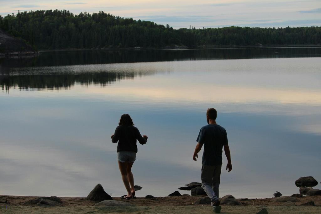 Two people walk towards a lake at dusk
