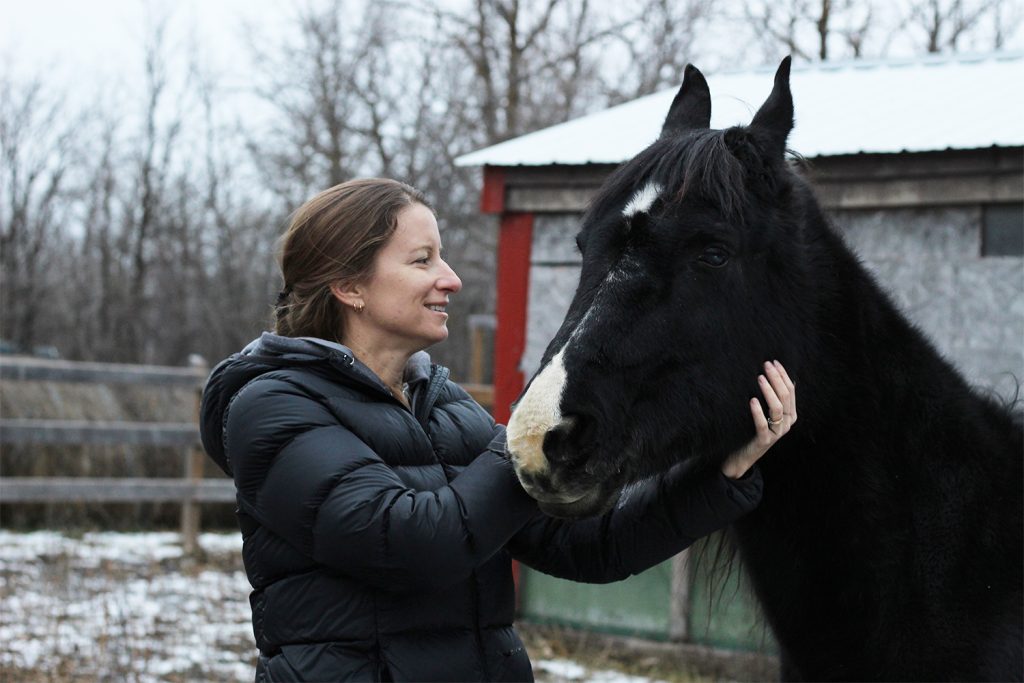 Cheryl pets a horse that's just above her height.