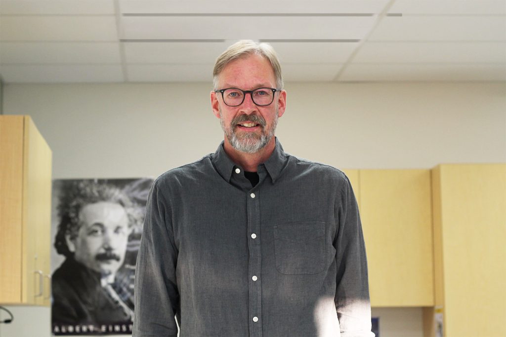 Ken poses for the camera in a classroom.