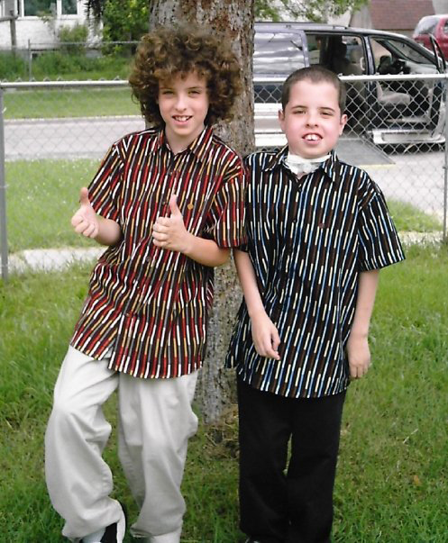 Logan and Robin Shaw outside their home wearing matching shirts. Robin has a tube attached to his throat.