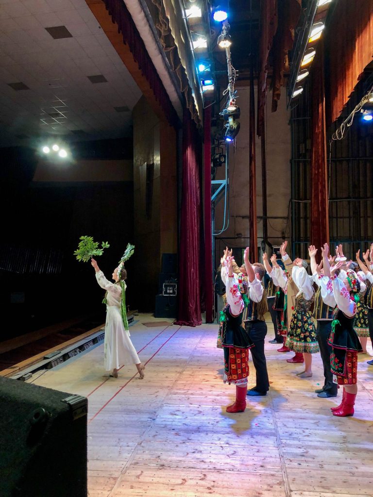 A group of dancers stands on stage with their arms in the air.