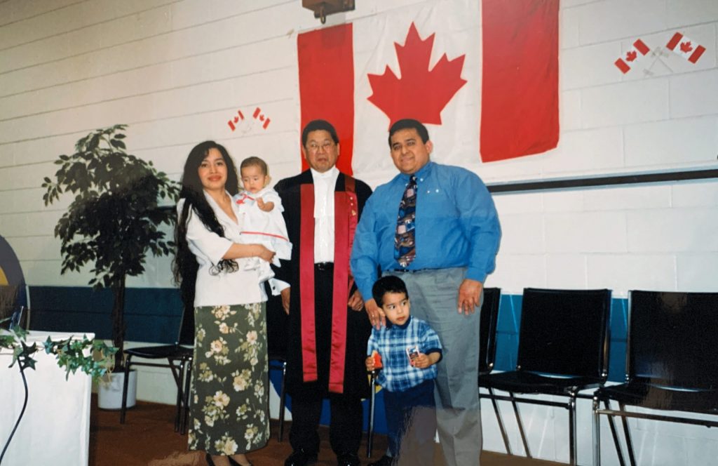 Oscar, Karen and their two children pose with a judge for the camera. A large Canada flag hangs on the wall behind them.