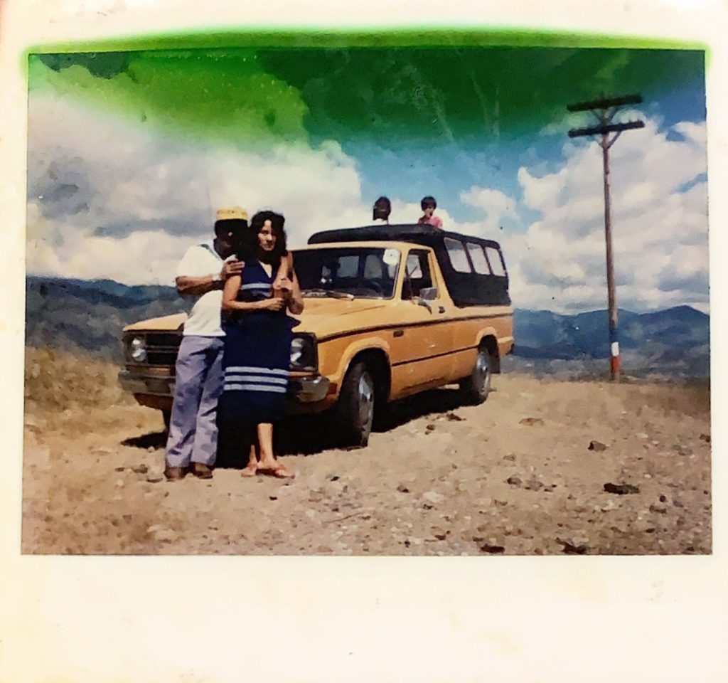 Oscar and Alicia stand in front of their truck. Standing in the bed of the truck are two children.