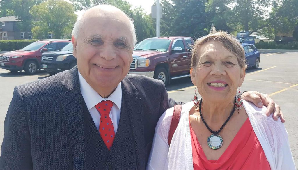 An elderly couple, dressed for church, smile at the camera.