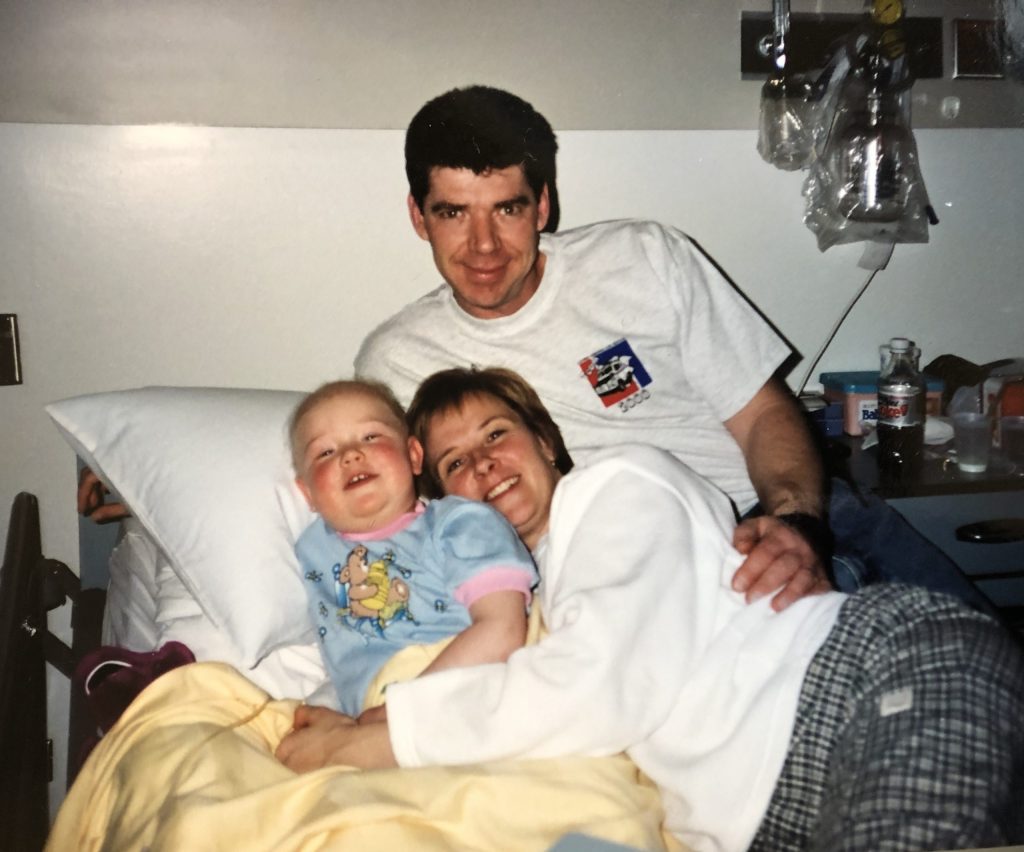 Sarah as a child smiling at the camera with her parents during her treatments.
