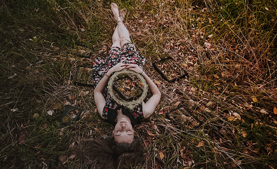 Sarah laying on the ground surrounded by 3 empty picture frames. She holds a gold frame on her chest that shows another empty picture frame.