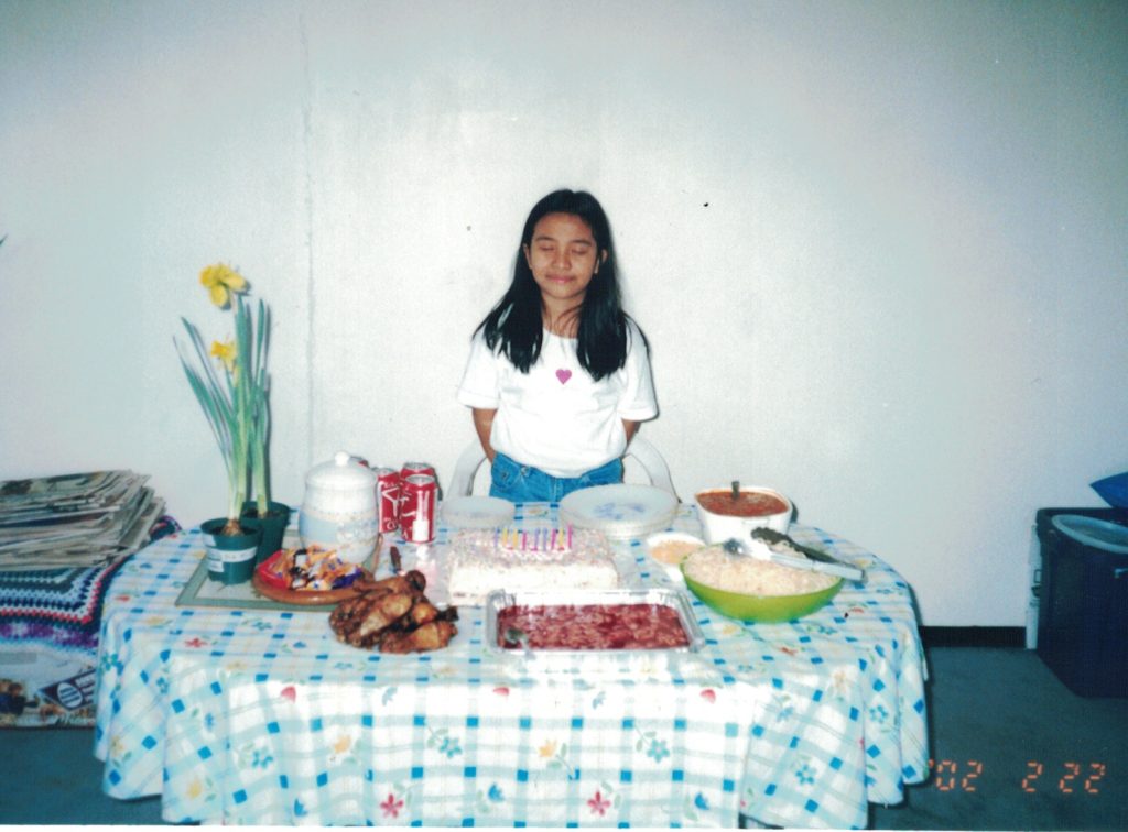 9 year old Alyssa stands in front of a table of food including a birthday cake.