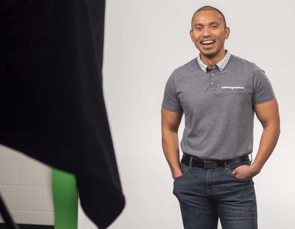 Randell Mauricio in front of a photo backdrop at WorkerBee.TV's studio.