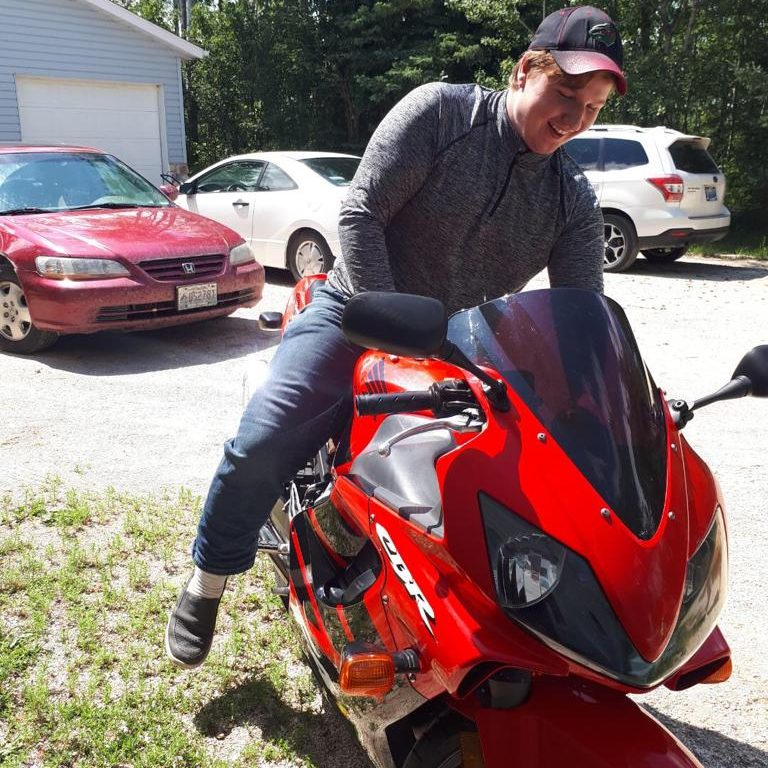 Ethan smiling while straddling a red motorcycle.
