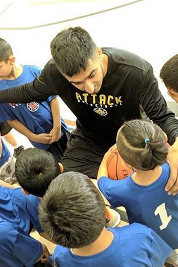 Raj surrounded by children in team jerseys. Raj's hand is on the should of one boy who is holding a basketball.