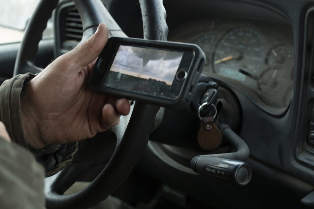 Man holds a phone showing the image of a tornado