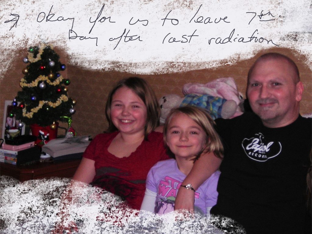 A picture of a man and two young girls sitting together on a couch in a room decorated for Christmas. Written on the picture is "Okay for us to leave 7th day after last radiation."