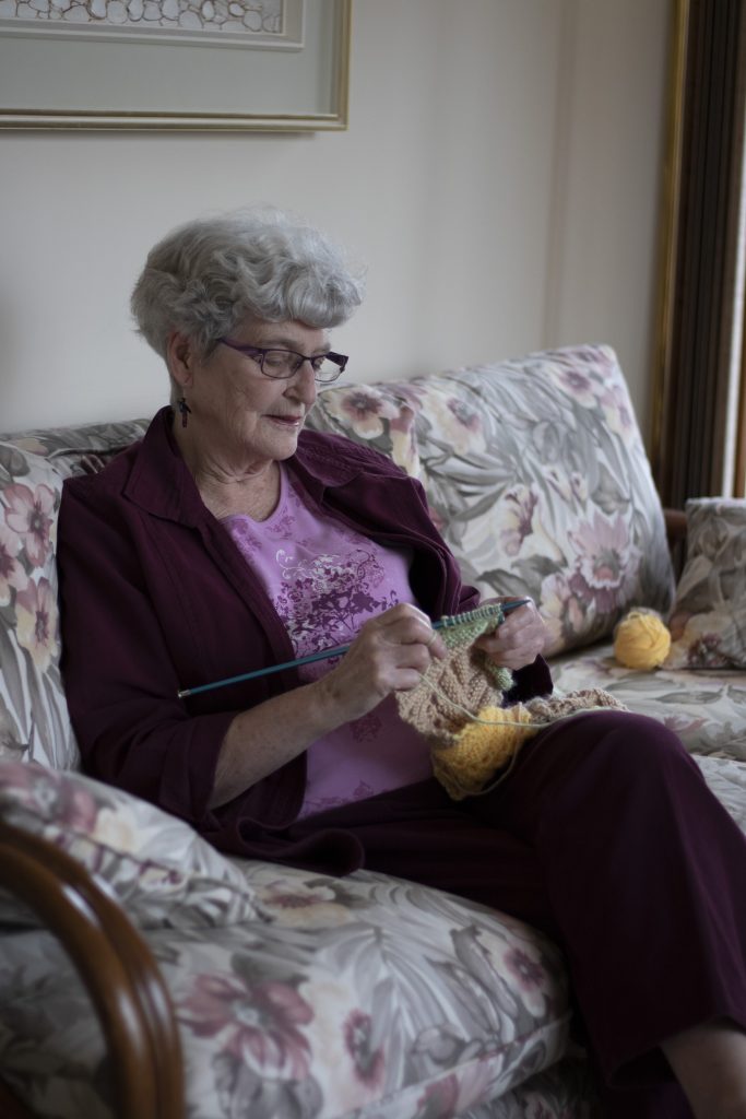 An old woman sits on a couch knitting.