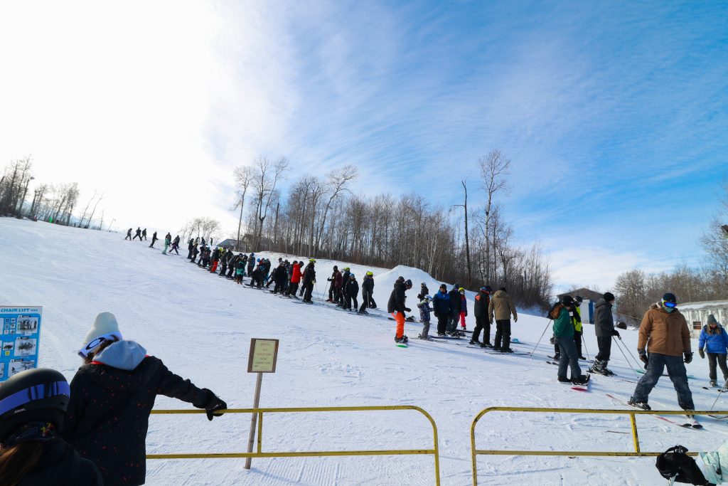 long line of skiers and snowboarders at chairlift at Asessippi