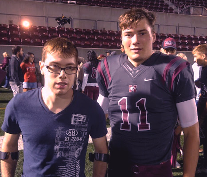 Caleb stands beside his brother Andre who is wearing his footbal uniform in a stadium.