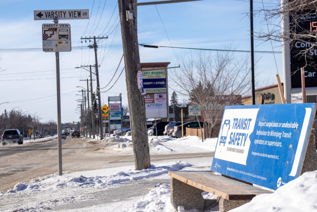 A bus bench covered with a Winnipeg Transit advertisement promoting transit safety.