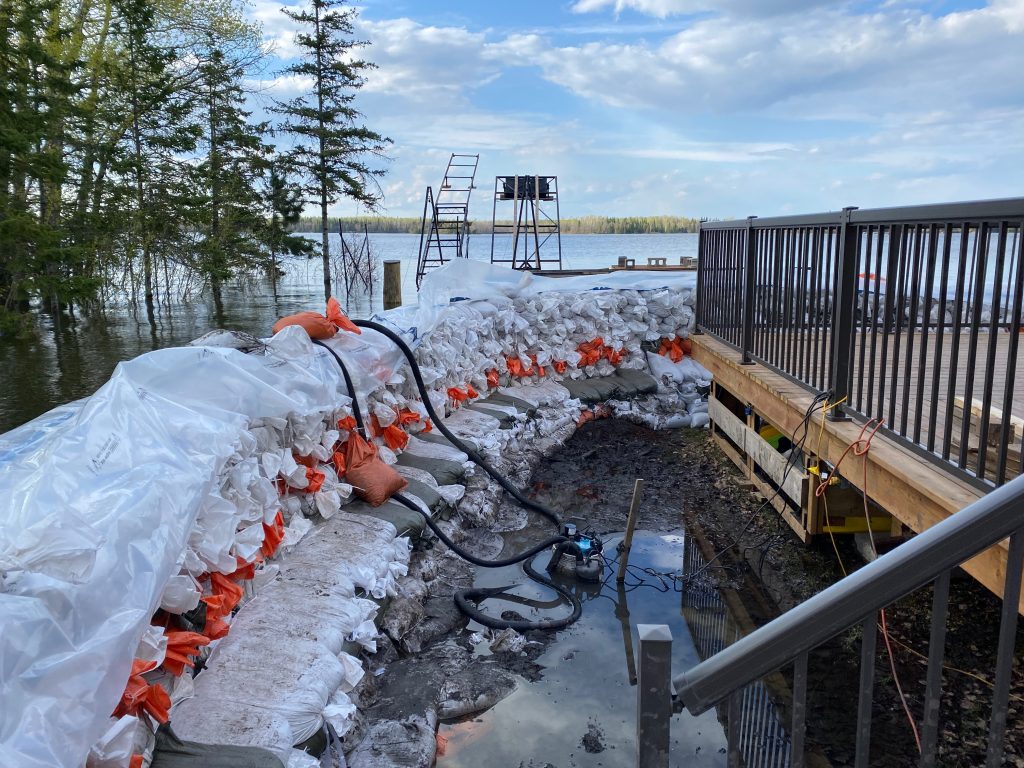 A photo facing the lake of Brent's dike with white and orange sandbags lining the side of the cabin.