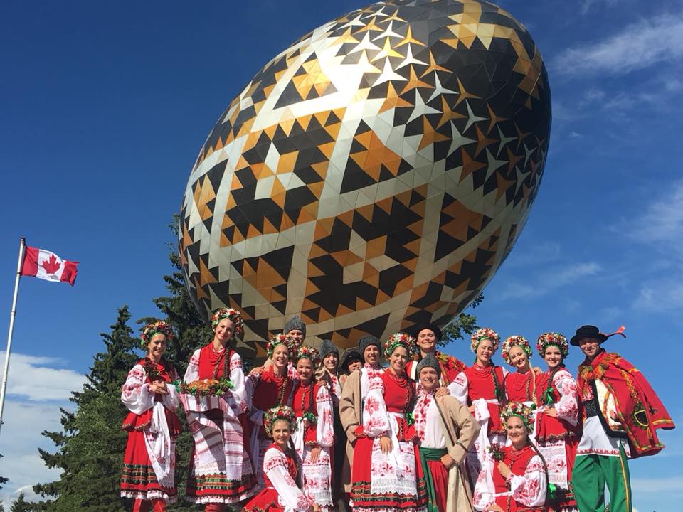 The Rusalka dancing group in their Ukrainian outfits standing in front of the Vegreville egg towering over them.