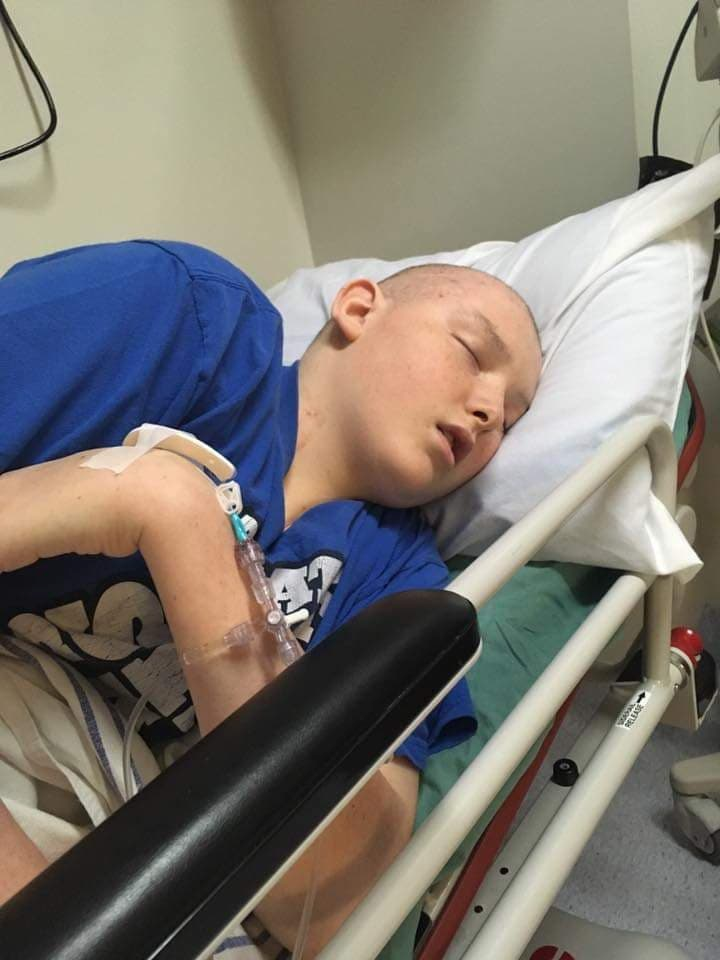 Ross laying in a hospital bed with an I.V. in his hand, visibly in pain. 