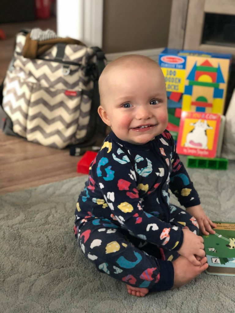 Malcolm, an infant, sitting on a rug smiling at the camera.