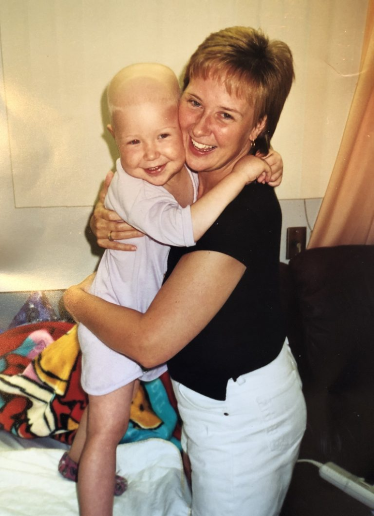 Sarah as a young child with no hair hugging her Mom as they both smile.