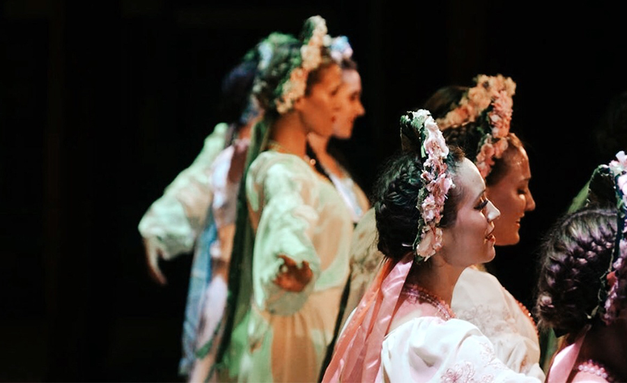 A photo of Liliya dancing with Rusalka on stage. They all wear Ukrainian blouses and flower headdresses.