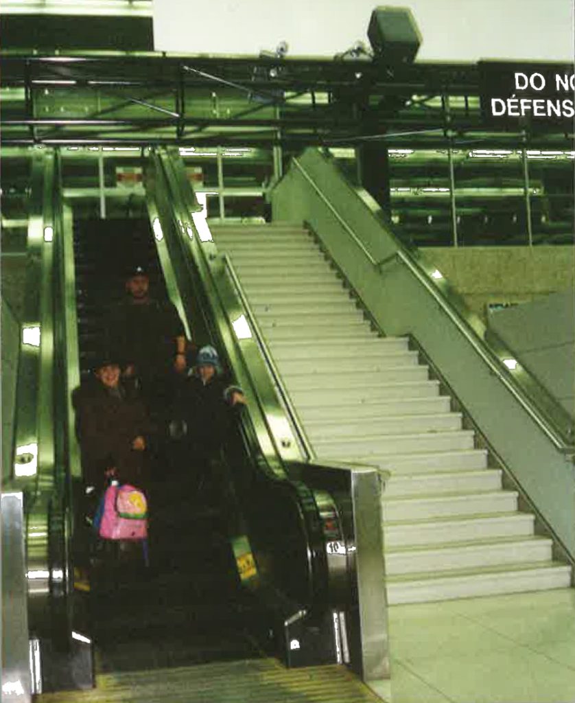 Liliya as a young girl with her parents standing on the escalator outside the airport.