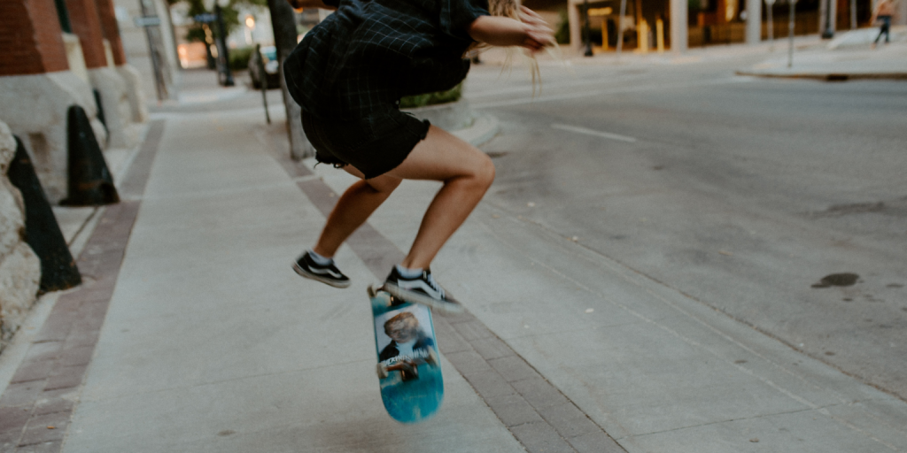 Photo of girl skateboarding on downtown sidewalk, doing a kick flip.