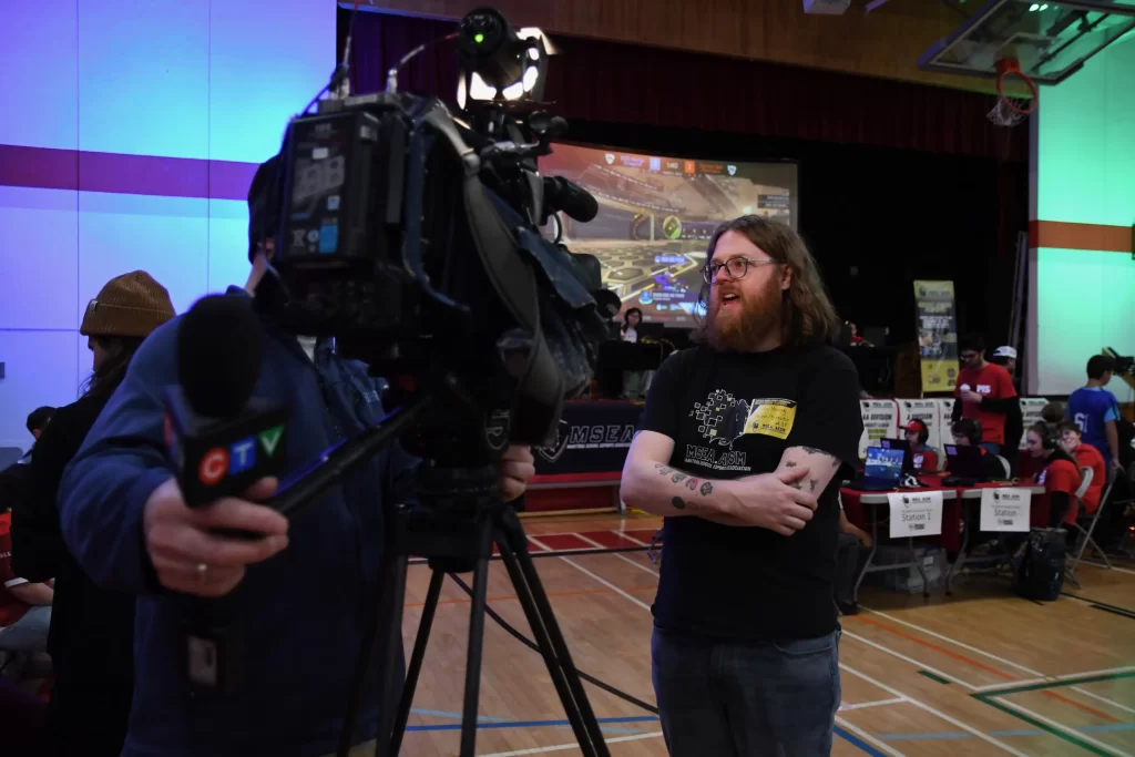 A news crew interviews an organizer on the gymnasium floor during the tournament.