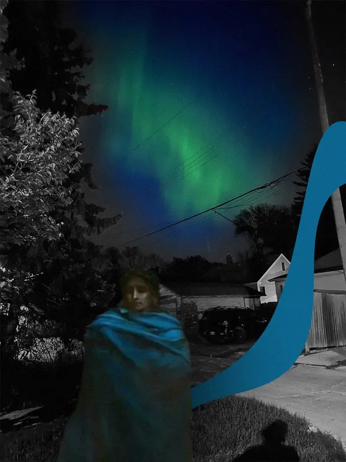 Virgil dressed in blue stands in a residential area beneath a sky coloured by aurora borealis.