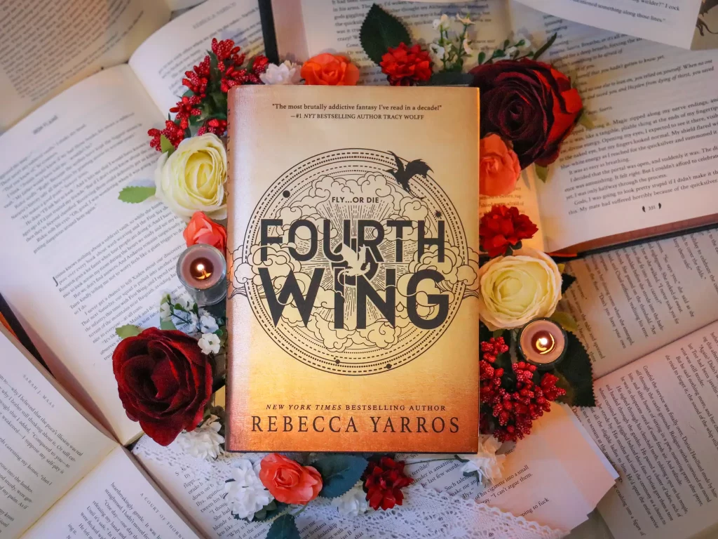The book Fourth Wing by Rebecca Yarros laying on a bed of open books and flowers.