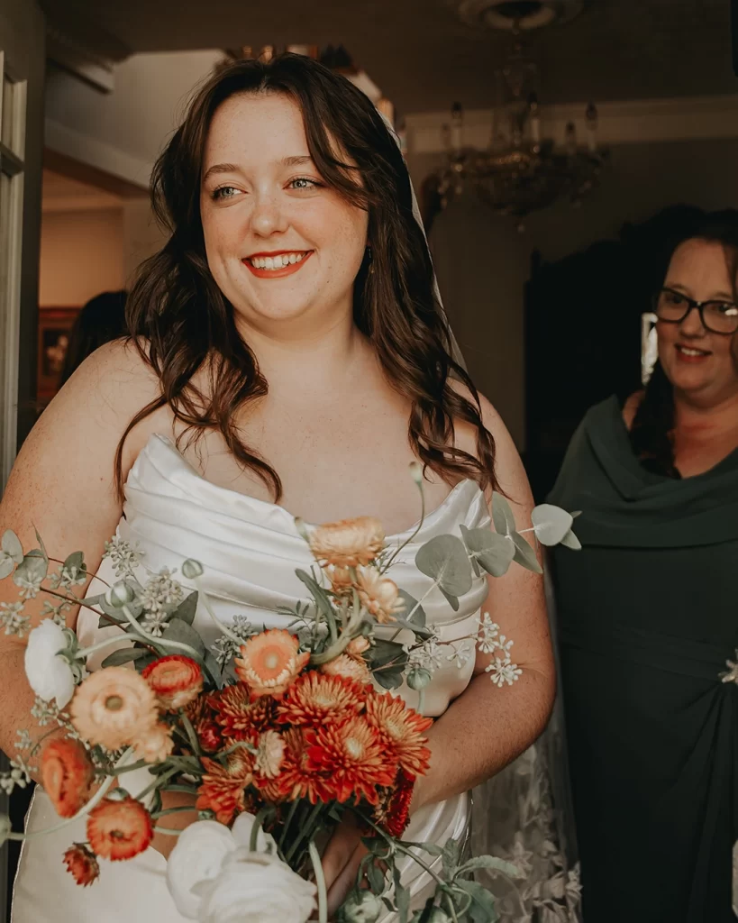 Abby is wearing a wedding dress and holding flowers