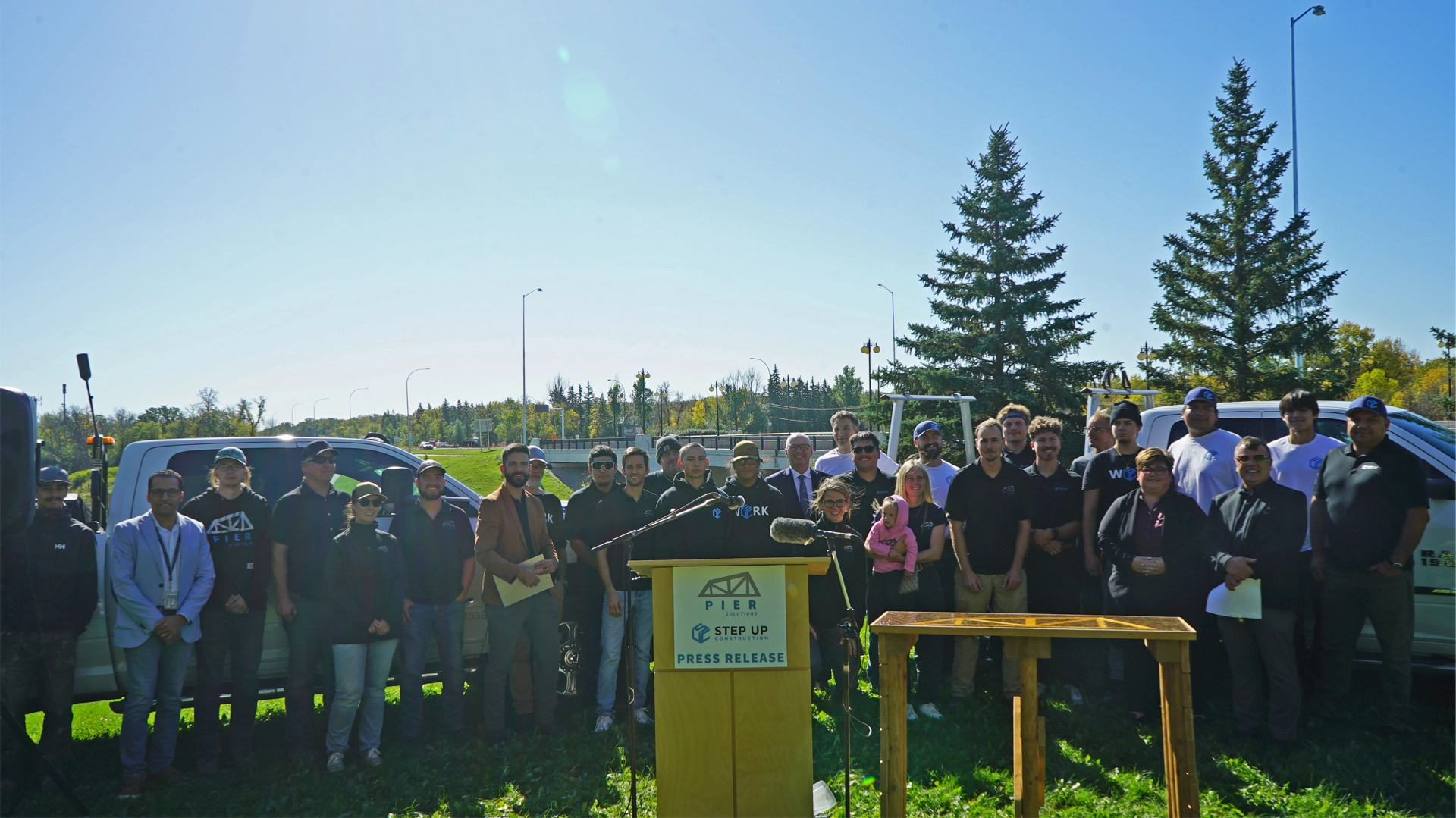 A large group of representatives, including Morley Daniels, stand behind the podium at the La Salle job site news conference. Mayor Scott Gillingham is in the centre.