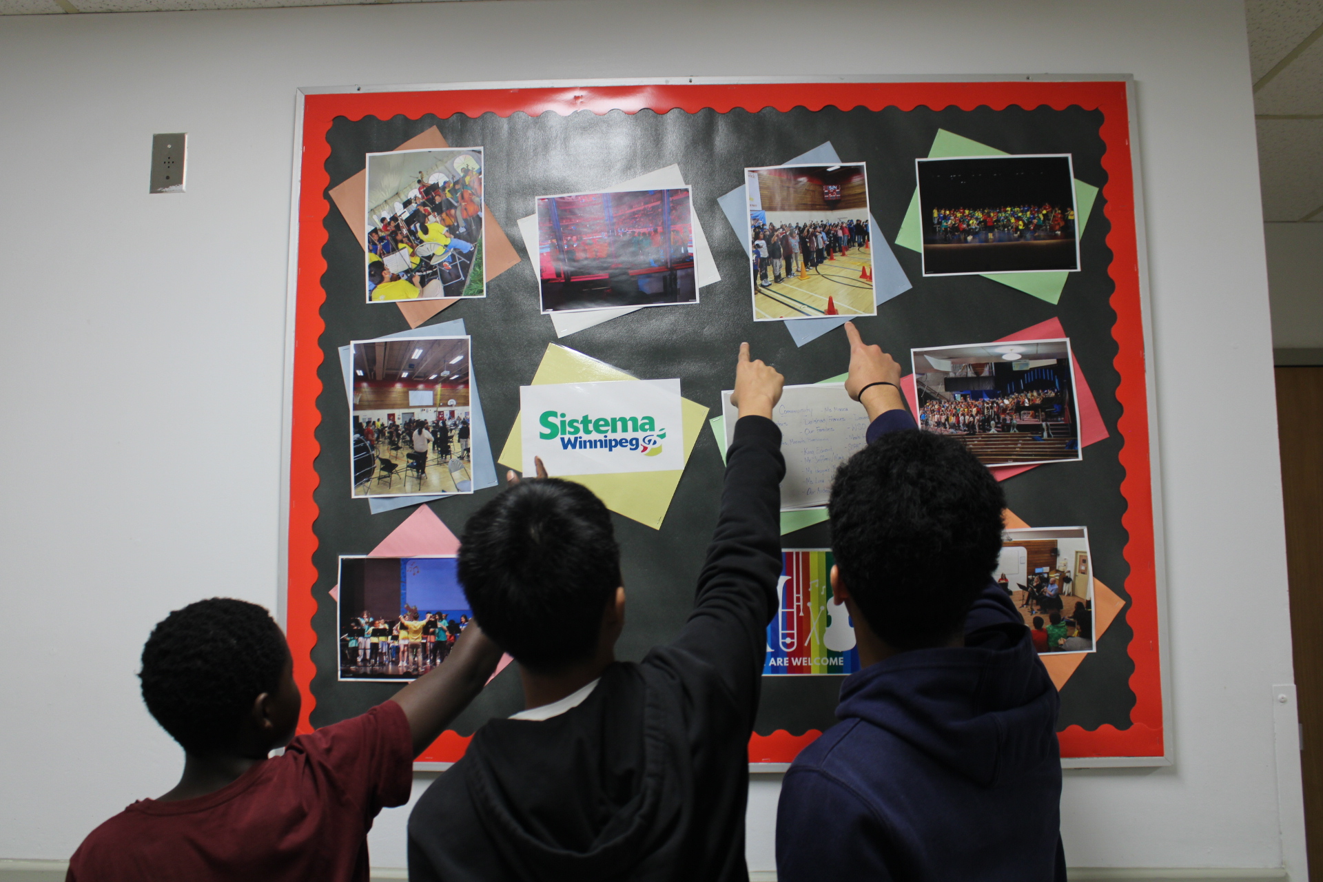 Three students pointing at pinboard in a school hallway. 
