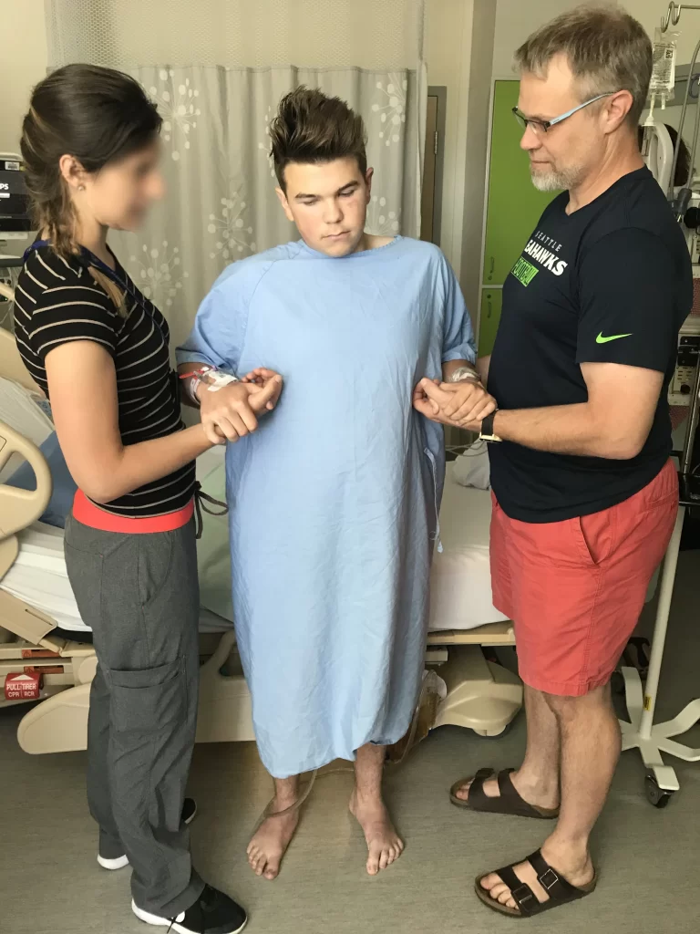 Spencer standing with the help of his dad and a physiotherapist