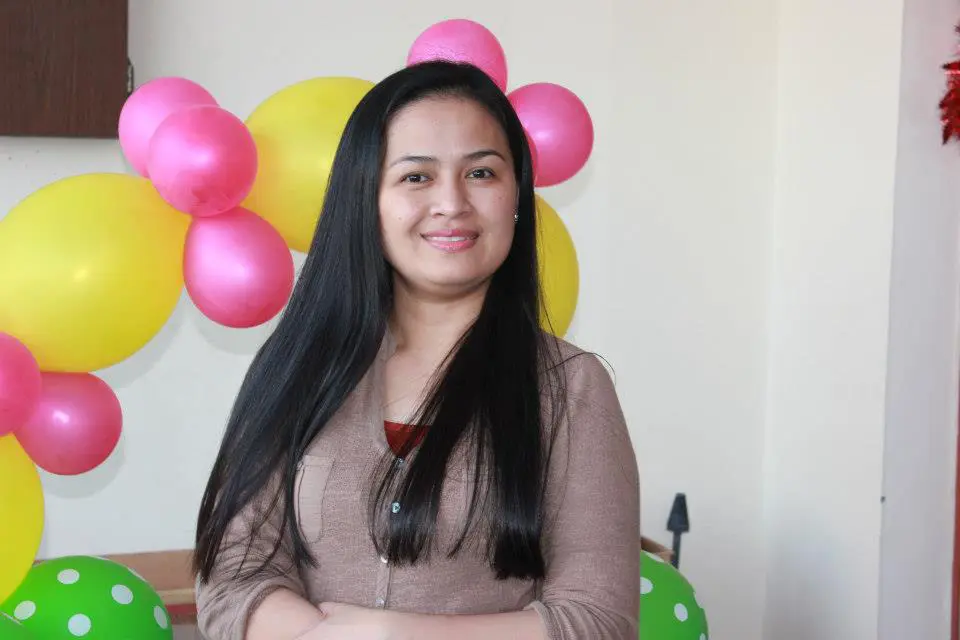 Woman in a church gathering. A multi coloured balloon arch behind her.