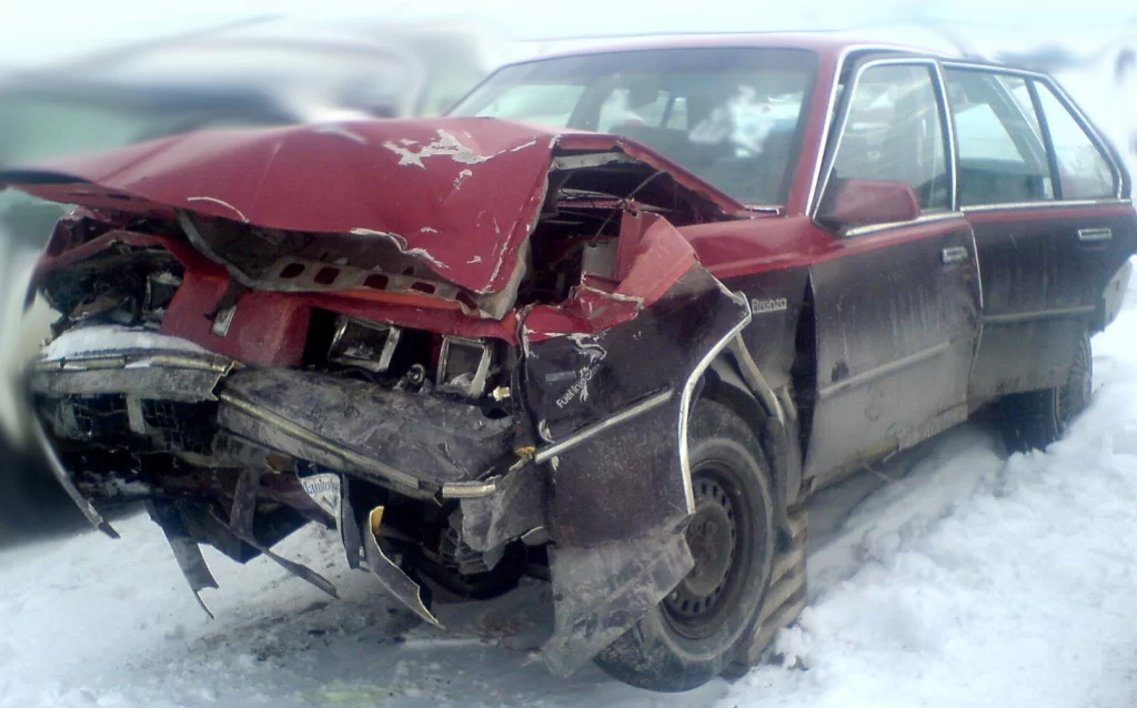 A 1985 Oldsmobile Firenza with a crushed hood and broken doors after a car accident.