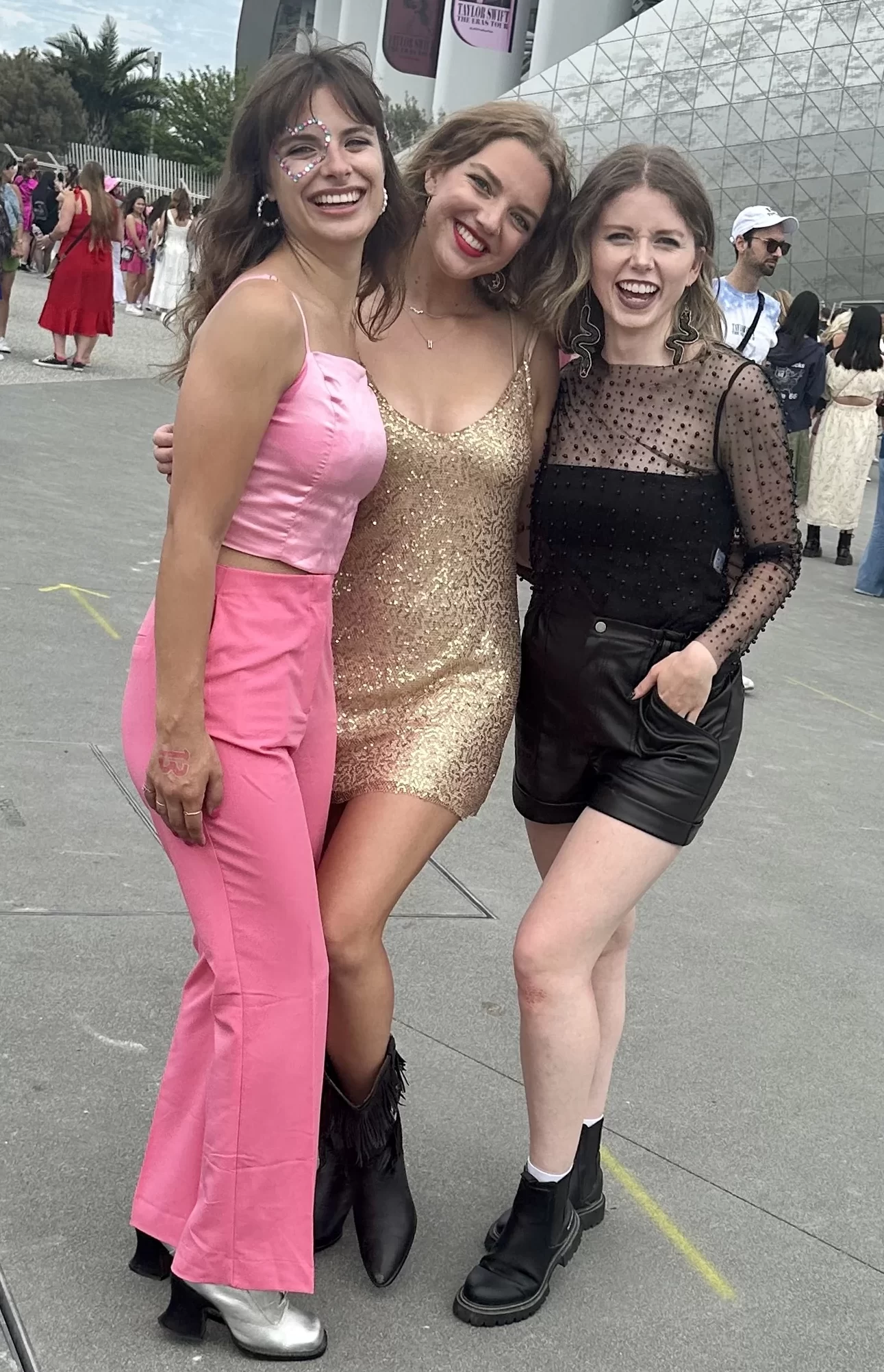 Three female friends standing outside of SoFi Stadium wearing pink, gold, and black