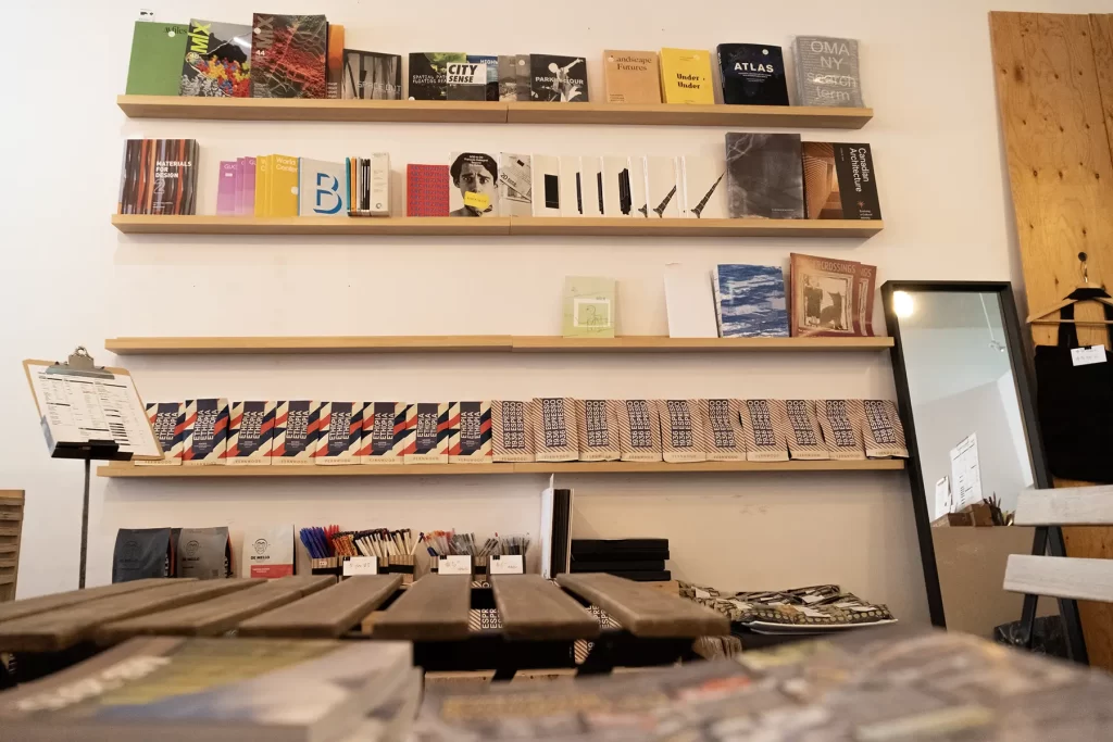 Two full shelves of books above an empty one and a shelf of coffee bags. A cafe table and more books are in the foreground.