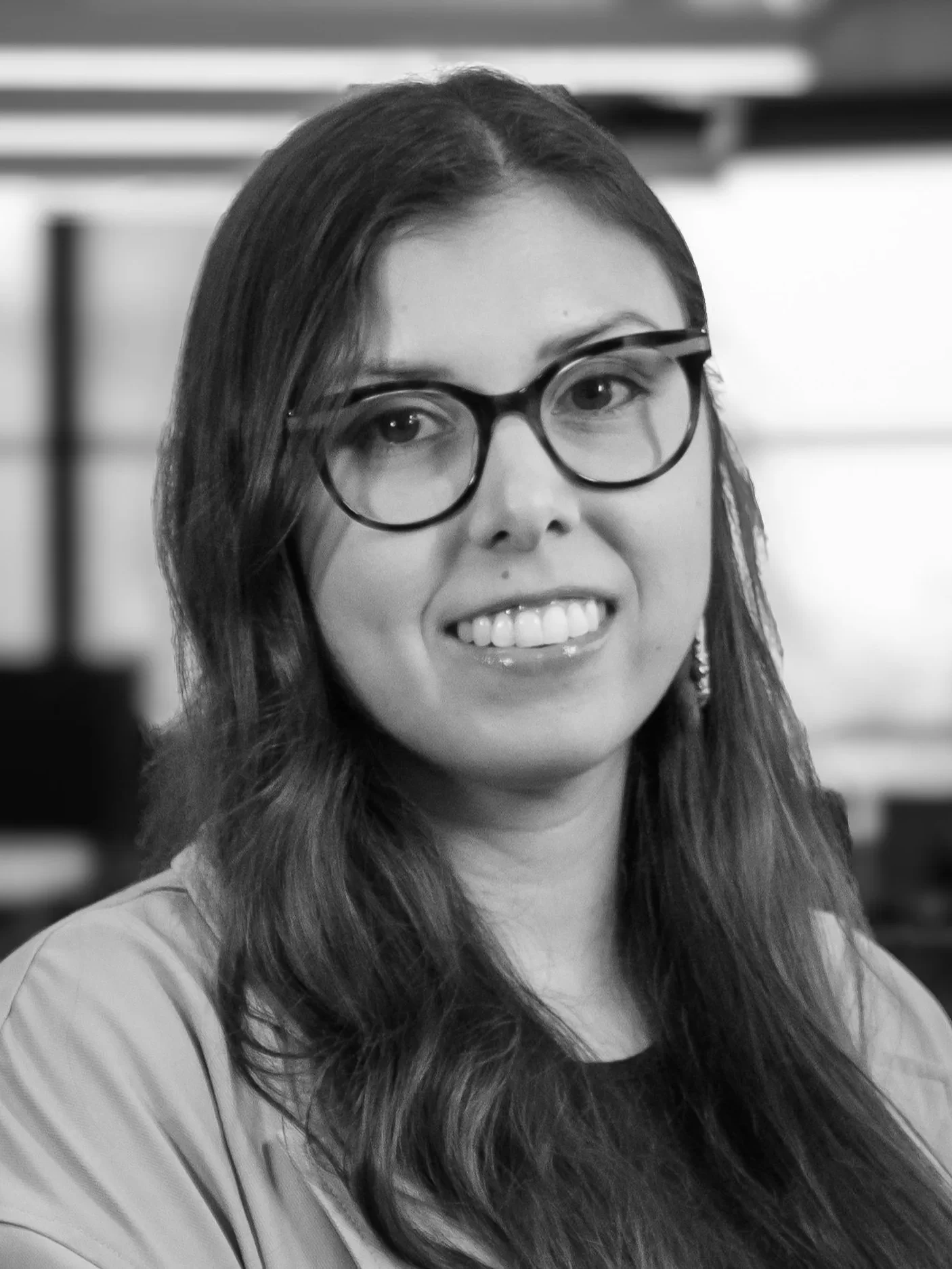 Danielle Desjarlais's headshot in grayscale. She is smiling and wears glasses with round frames. Her long wavy dark hair rolls over her shoulders.