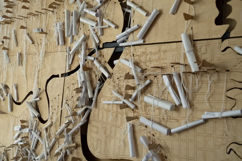 Rolled up notes are pegged to a wooden map of Winnipeg with rivers cut out and streets etched into the surface.
