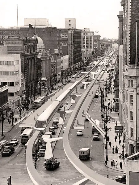 A three-car monorail rides on one of two parallel tracks suspended above Portage Avenue superimposed on a black and white photo from the early 1970s.